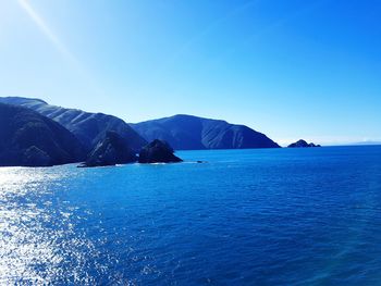 Scenic view of sea and mountains against clear blue sky