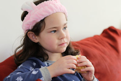 Cute little girl in a pink head dress is eating crepes on the couch