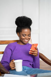 Woman holding coffee cup using smart phone at home