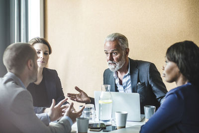 Businessman discussing strategies with coworkers while sitting in board room during meeting