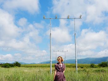 Portrait of young woman standing on field against sky