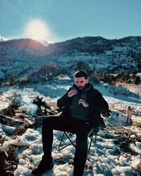 Portrait of young man sitting on snow covered landscape