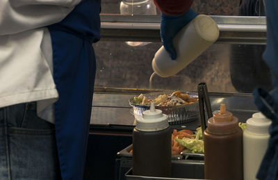 Midsection of men pouring sauce over food at concession stand