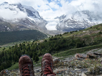 Low section of person on snowcapped mountain against sky