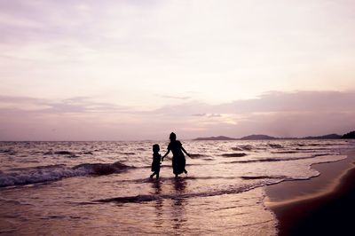 Silhouette men on beach against sky during sunset
