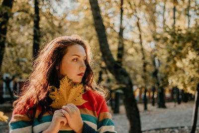 Beautiful woman holding leaf against trees