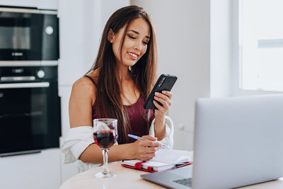 Young woman using phone while sitting on table