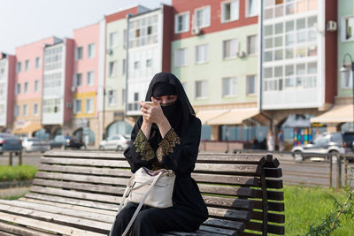 Muslim woman paints her eyes and eyebrows while sitting on the street.