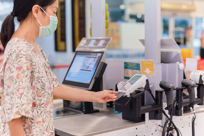 Woman with bank card paying food at grocery store self-checkout.