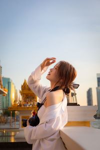 Side view of woman with arms raised standing against sky