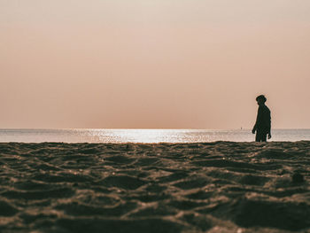 Man standing on beach against clear sky during sunset