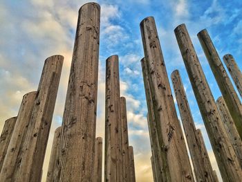 Low angle view of wooden posts against cloudy sky