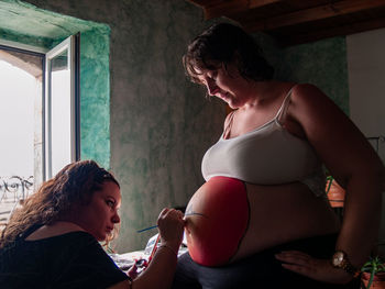 Friend painting stomach of pregnant woman at home