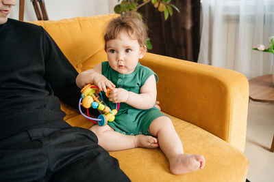 Young dad plays with his baby son on a yellow sofa