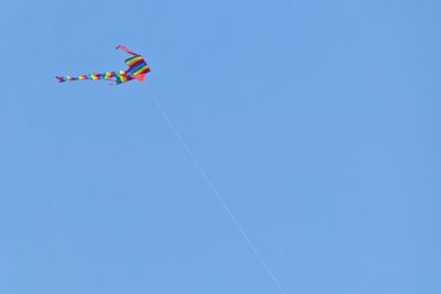 Low angle view of multi colored kite against clear blue sky