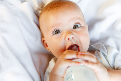 Cute baby girl drinking milk while lying on bed