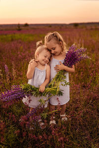 Two little sisters hugging each other in a field with flowers in their hands