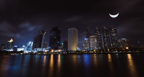 Illuminated city by river against sky at night