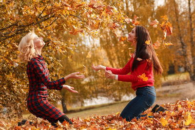 Happy friends playing with autumn leaves at park