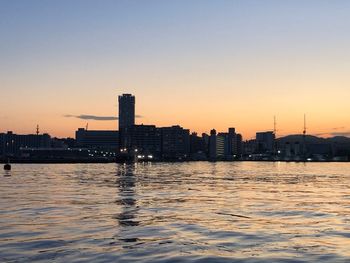 Sea and buildings against clear sky during sunset