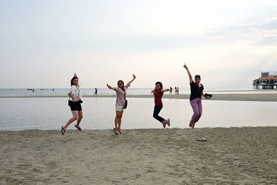 People jumping on beach against sky