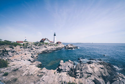 Lighthouse amidst sea and buildings against sky