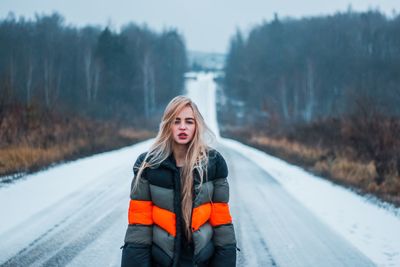 Portrait of young woman standing on road during winter