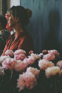 Woman looking away by pink flowers against wall