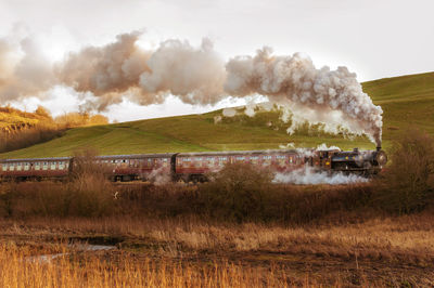 Heritage steam train passing by landscape against sky