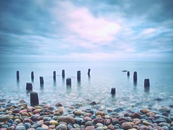 Wooden posts in sea against sky