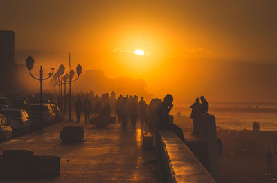 Silhouette people by sea against sky during sunset