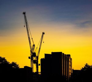 Silhouette cranes at construction site against sky during sunset