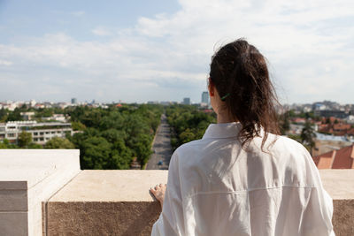 Rear view of man looking at cityscape against sky