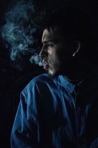 Young man exhaling smoke against black background