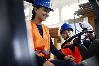 Man instructing female worker on forklift in factory