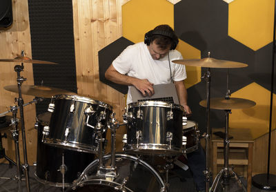 White caucasian man connects drums, musical instrument and app on notebook, makes equipment setup in