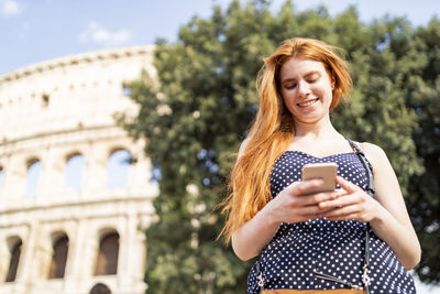 Happy young woman using smartphone near tourist attraction