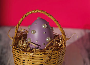 Homemade purple easter egg in easter basket 
on white table with pink background