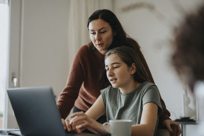 Girl using laptop sitting by mother at modern home