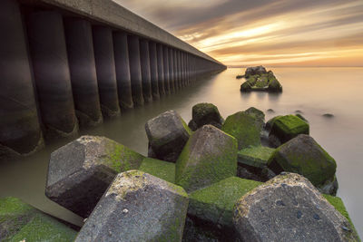 Rocks by sea against sky during sunset