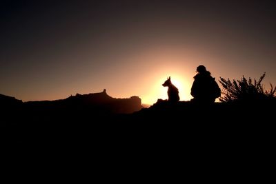 Silhouette woman and dog sitting against sky during sunset