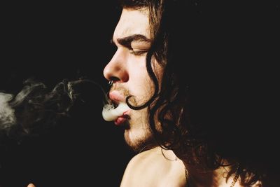 Portrait of young man smoking cigarette against black background