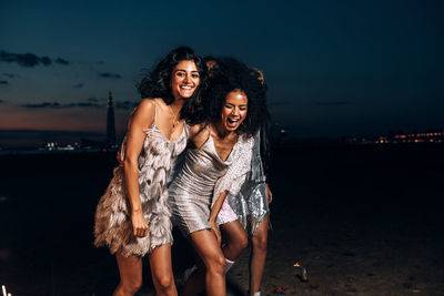 Young woman smiling while standing on beach against sky at night