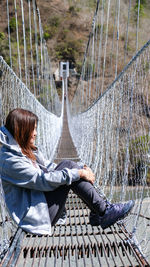 Side view of woman sitting on footbridge