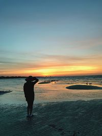 Rear view of silhouette woman standing at beach during sunset