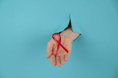 A woman's hand with a red bow sticks out of a hole in a blue background. 