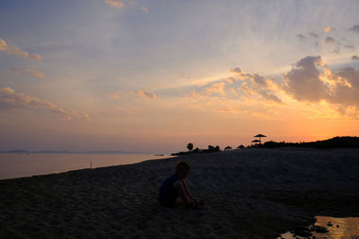 People sitting on beach by sea against sky during sunset