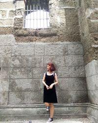 Full length of young woman looking away while standing against wall