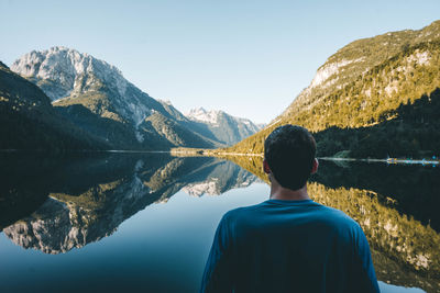 Rear view of man looking at lake against mountain