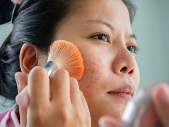 Close-up of woman applying makeup against wall